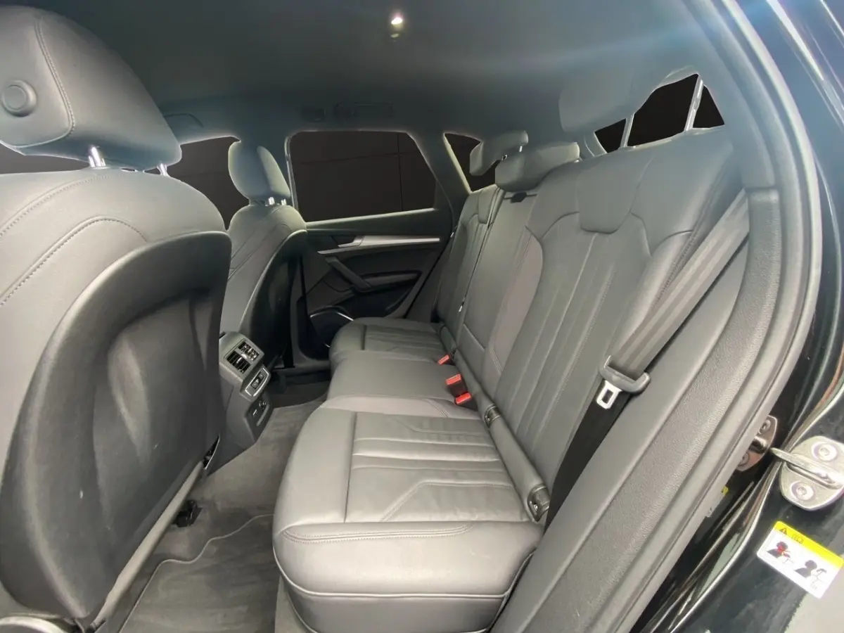 Vue intérieure côté droit sur la banquette arrière en cuir gris du SUV Audi Q5 noir, avec accoudoir central et ceintures visibles.