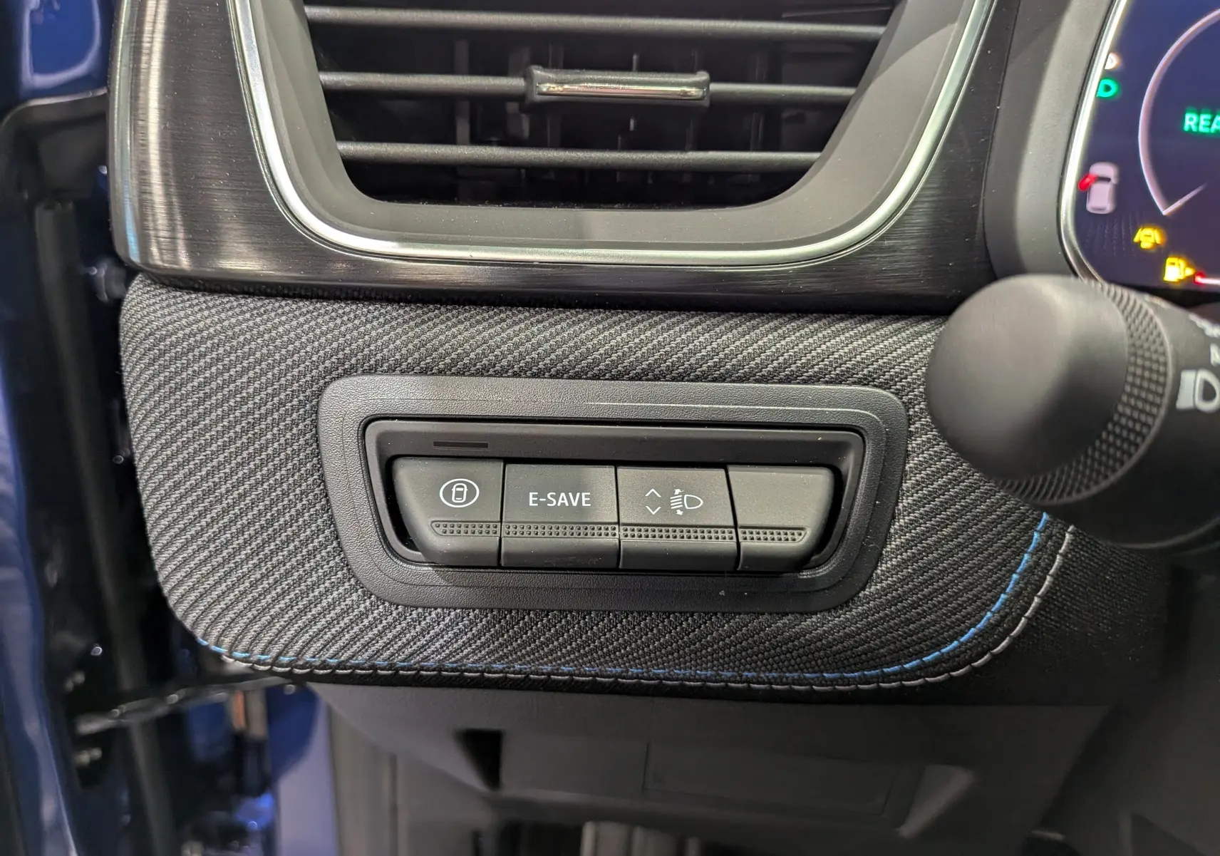 Gros plan sur les commandes sous la sortie d'air côté gauche du tableau de bord du Renault Captur E-Tech bleu Iron avec surpiqûres bleues.