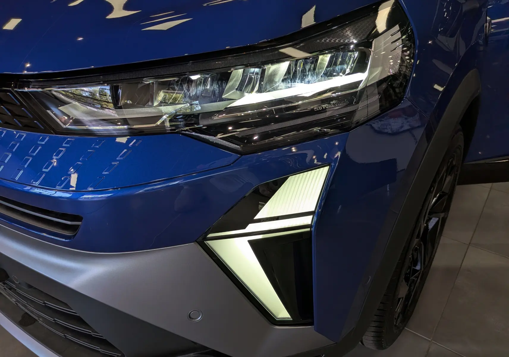 Gros plan sur le phare avant droit allumé du Renault Captur E-Tech bleu Iron avec détails lumineux distinctifs.