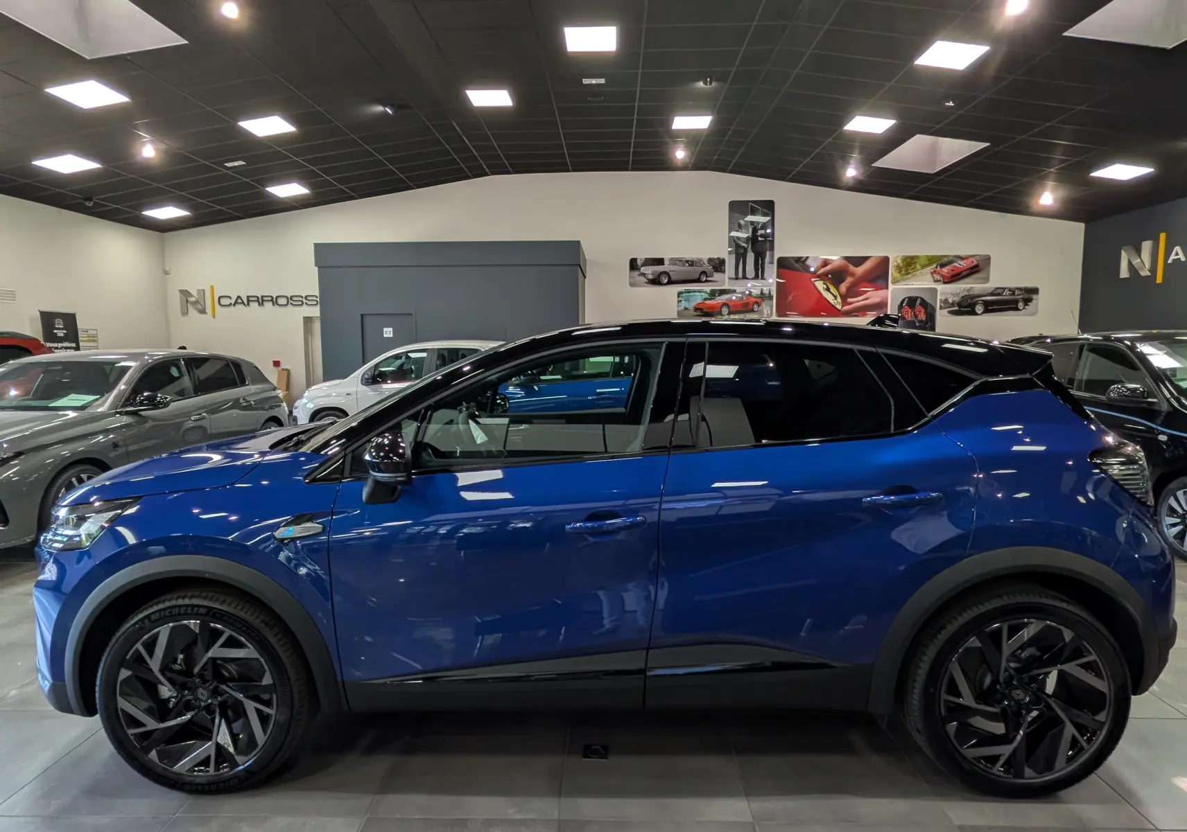 Profil côté gauche du Renault Captur E-TECH hybride bleu Iron avec toit noir, jantes noires et intérieur visible en showroom.