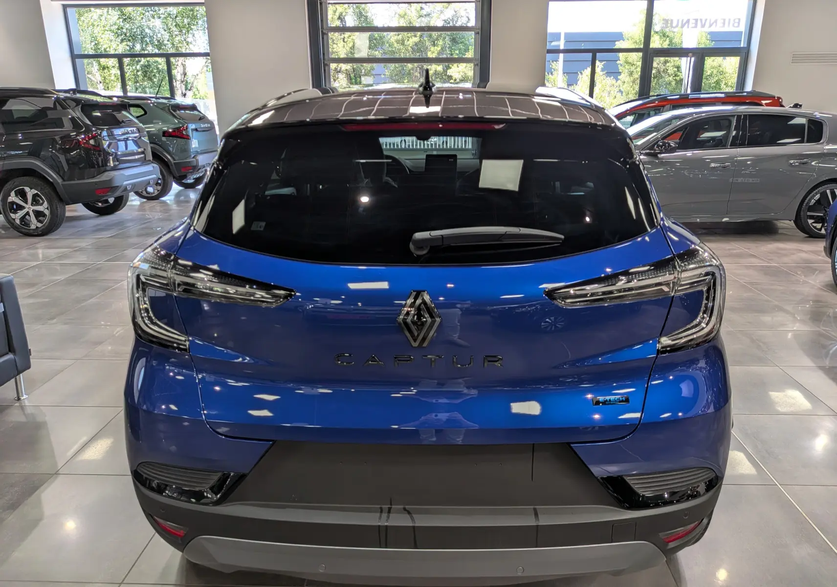 Vue arrière d’un Renault Captur E-TECH hybride bleu Iron avec toit noir, dans un showroom lumineux.