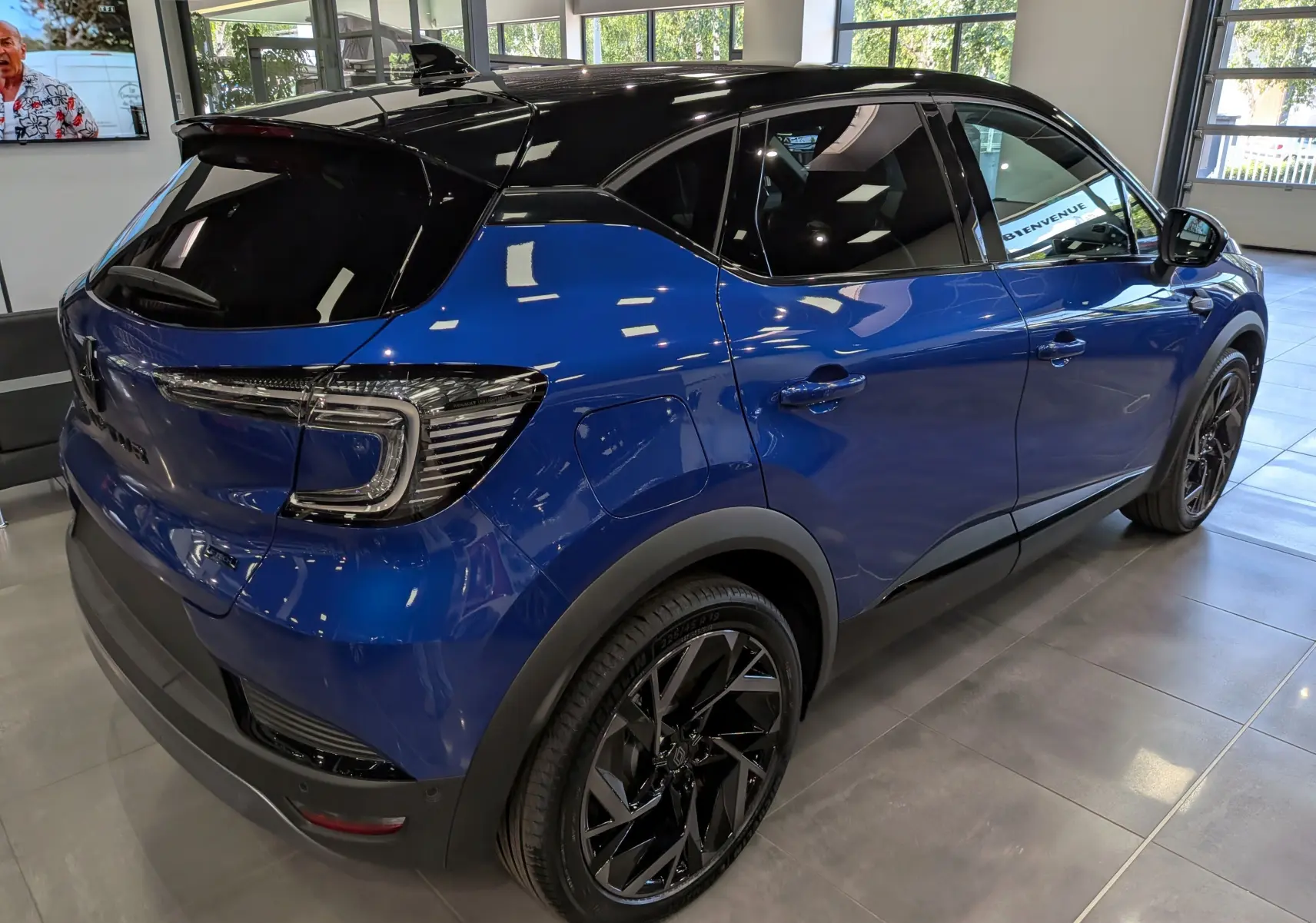Vue 3/4 arrière droite d’un Renault Captur E-TECH hybride bleu Iron avec toit noir et jantes noires en showroom.