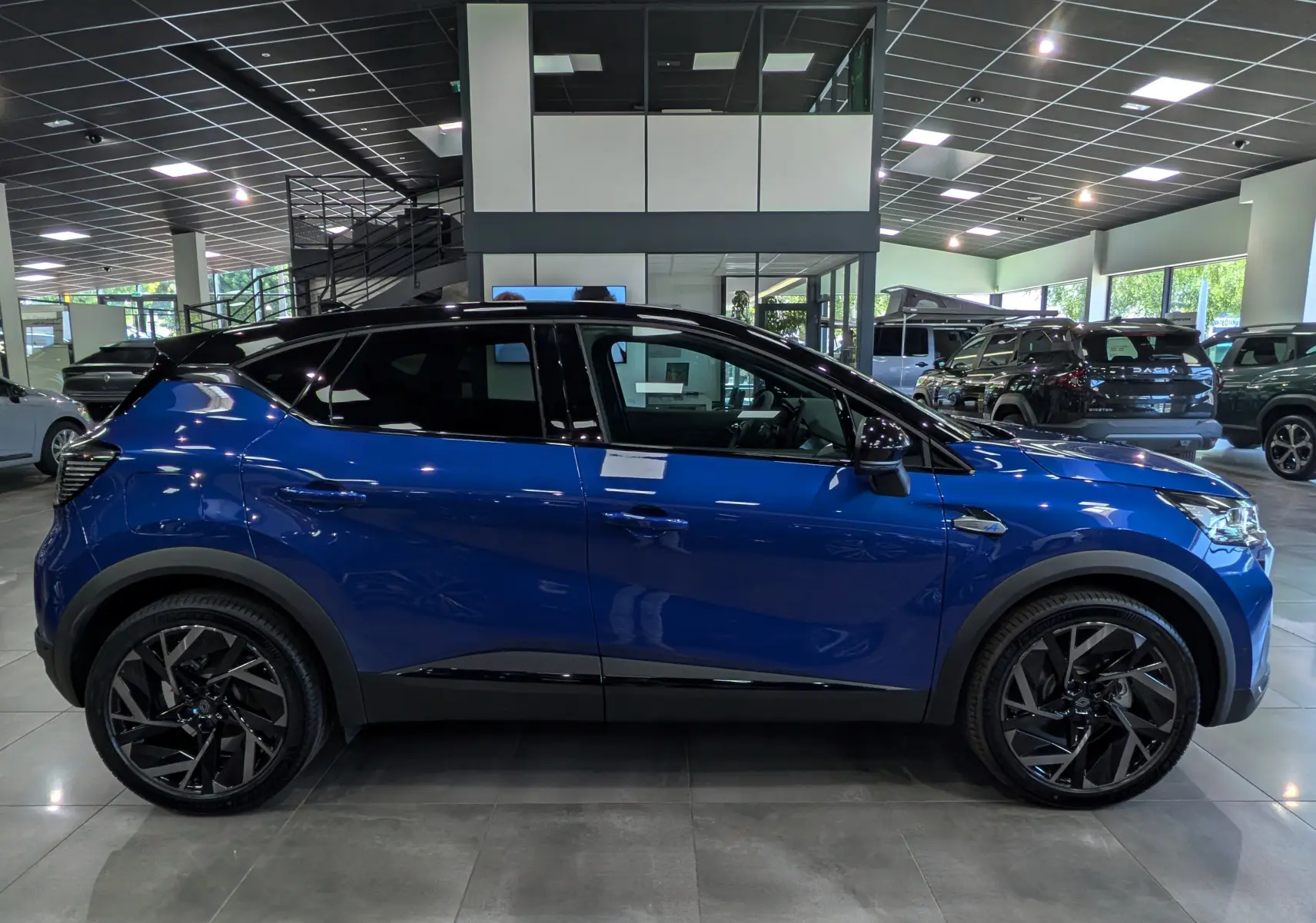 Profil côté gauche du Renault Captur E-TECH hybride 2026 en Bleu Iron avec toit noir et jantes noires en showroom.