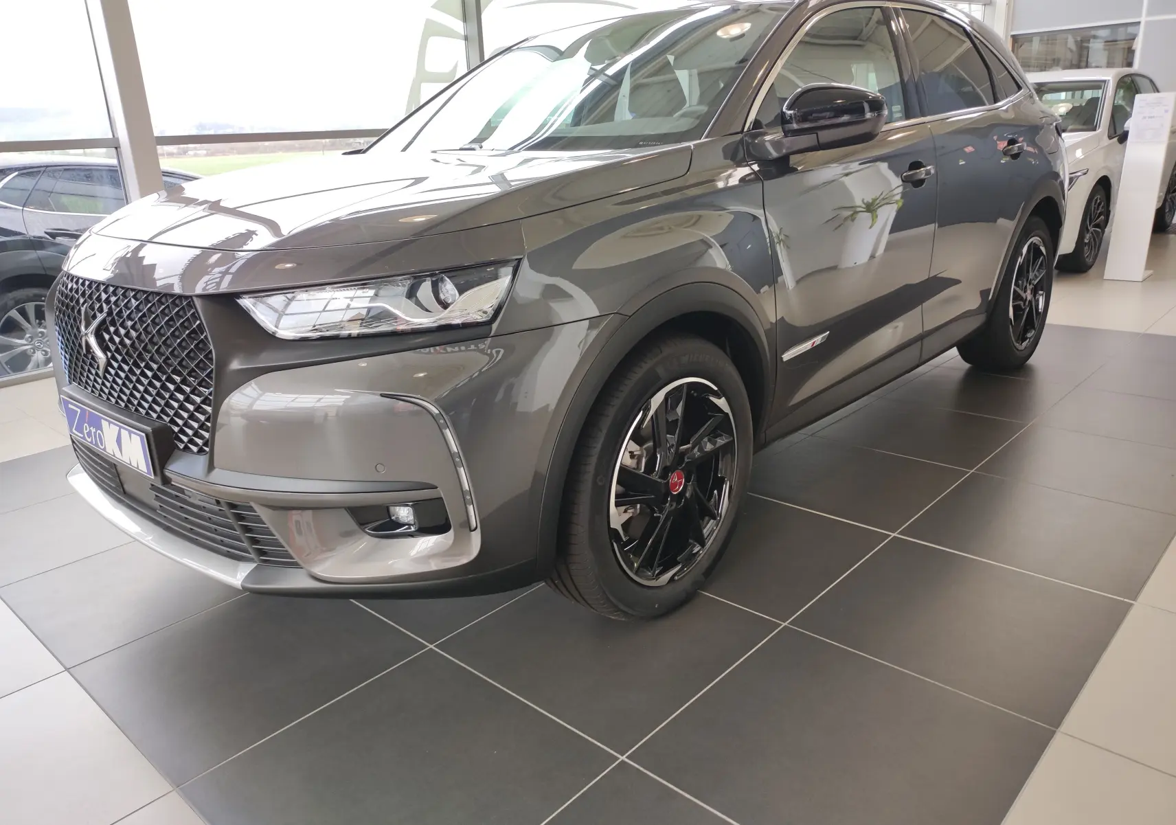 Vue 3/4 avant droit du DS7 Crossback E-TENSE gris 2022 avec jantes noires et calandre distinctive en losange.