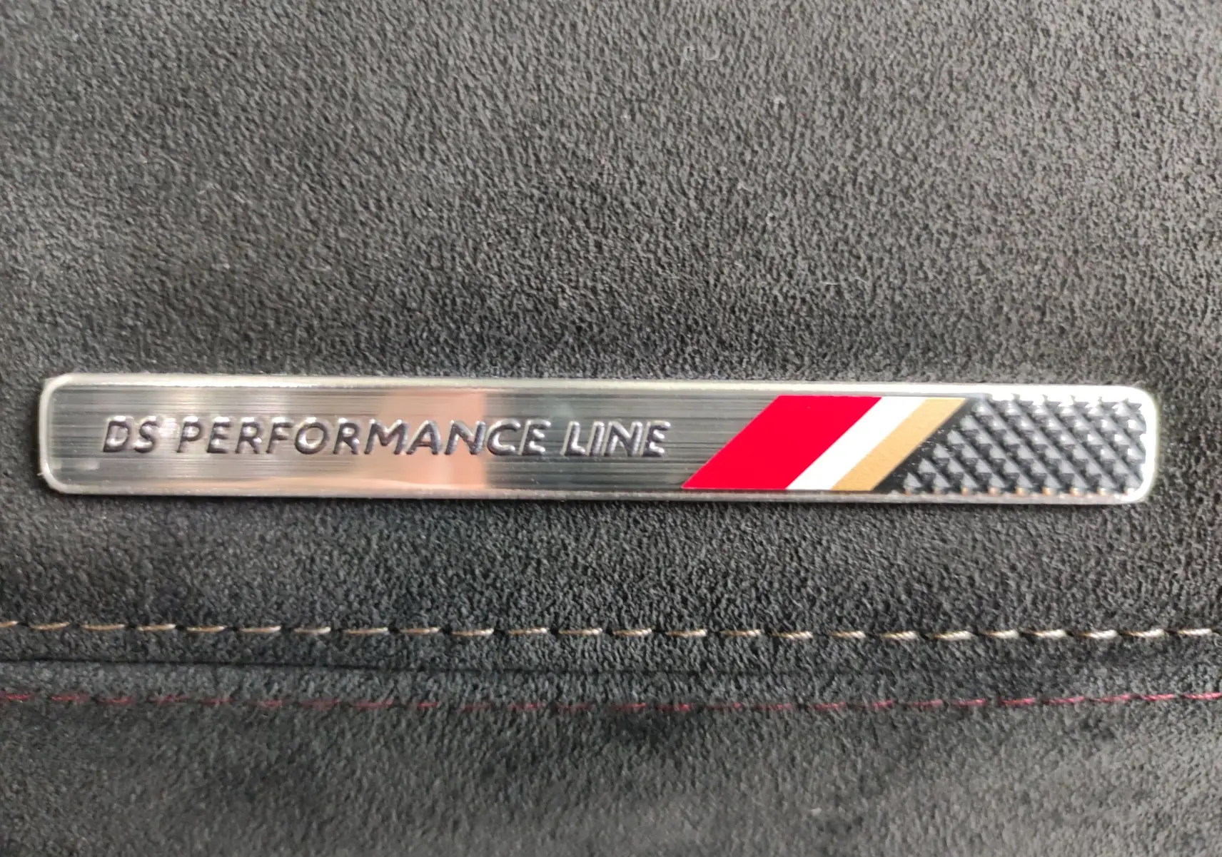 Gros plan sur l’inscription DS Performance Line sur une plaque métallique intégrée dans un revêtement noir intérieur.