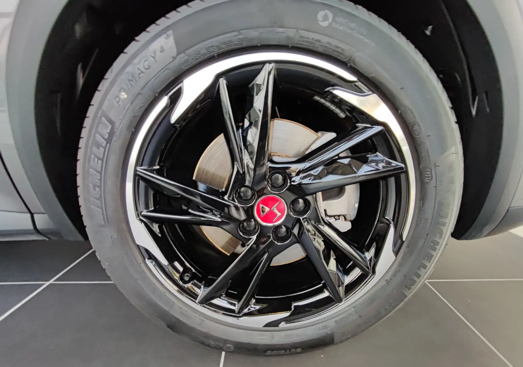 Gros plan sur la jante noire brillante avec logo DS rouge du DS7 Crossback E-TENSE gris, roue avant droite visible.