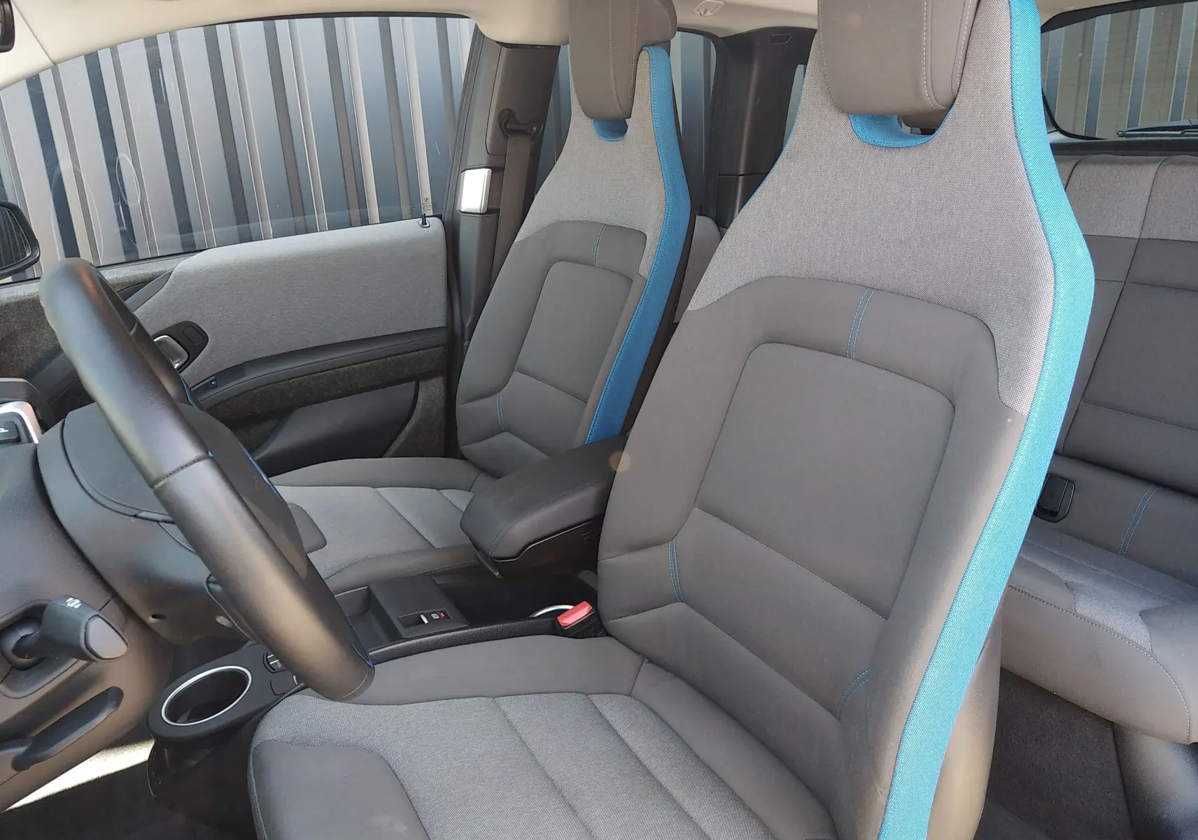 Intérieur avant de la BMW i3 bleu, sièges tissu gris avec surpiqûres et contours bleus, volant cuir noir visible côté gauche.