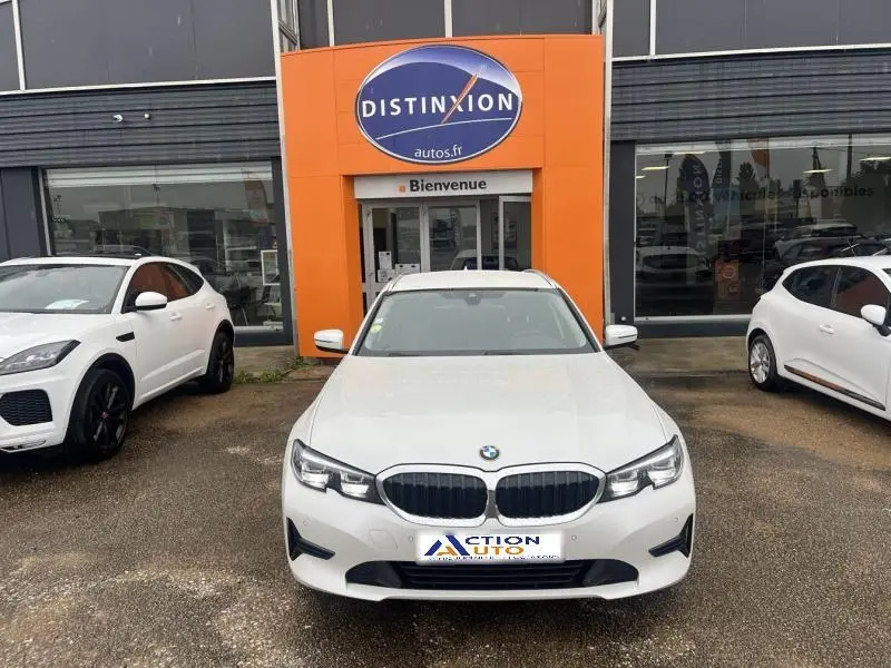 BMW Série 3 316dA blanche vue de face, stationnée devant un bâtiment avec enseigne orange Distinxion.