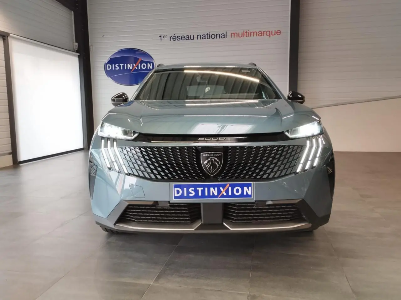 Vue avant du Peugeot 5008 2025 bleu Ingaro avec calandre noire et feux LED à griffes allumés en showroom.