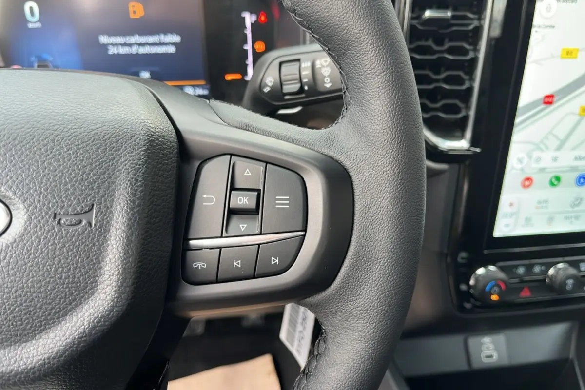 Gros plan sur le volant cuir multifonctions du Ford Ranger 2025, avec commandes intégrées et écran tactile visible en arrière-plan.