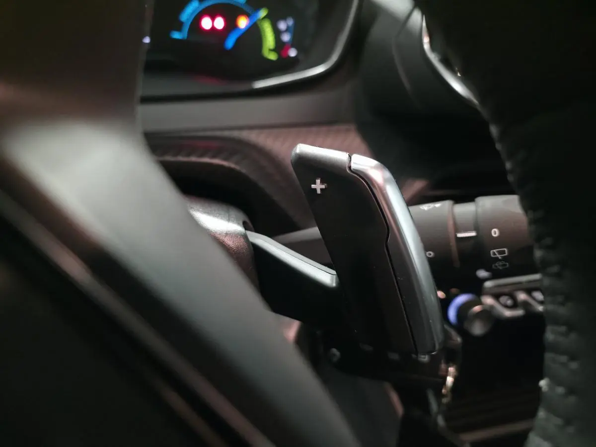 Gros plan sur la palette de changement de vitesse "+" derrière le volant du Peugeot 2008 gris, intérieur sombre.