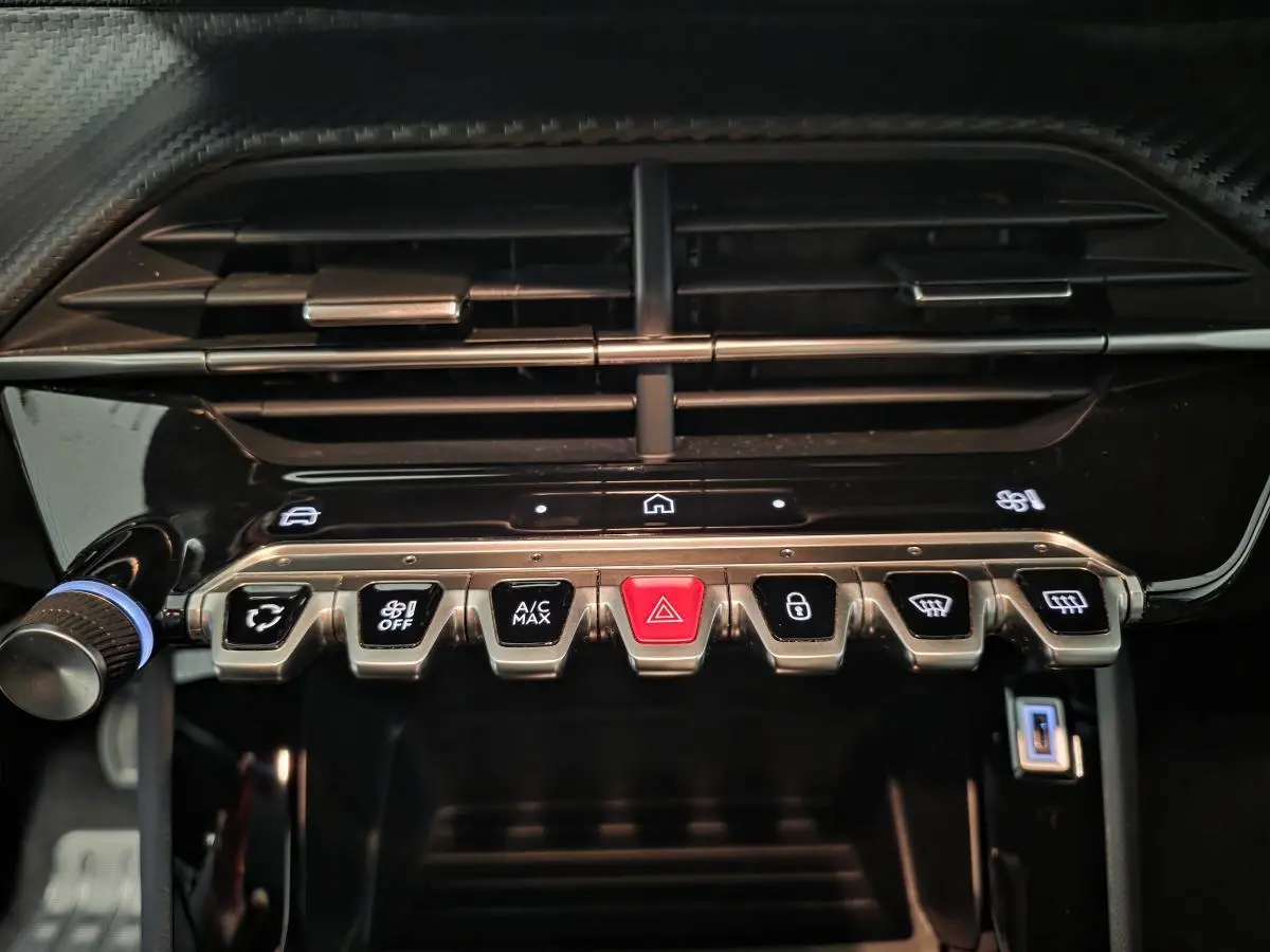 Gros plan sur la console centrale de la Peugeot 2008 2025, boutons métalliques et finition noire brillante.