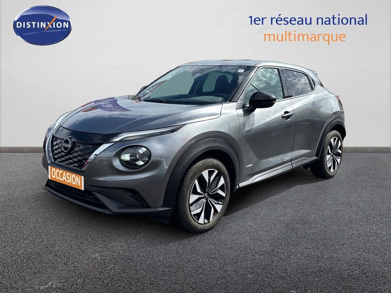 Nissan Juke Hybrid gris squale métal en 3/4 avant droit, avec jantes distinctives et calandre noire brillante.
