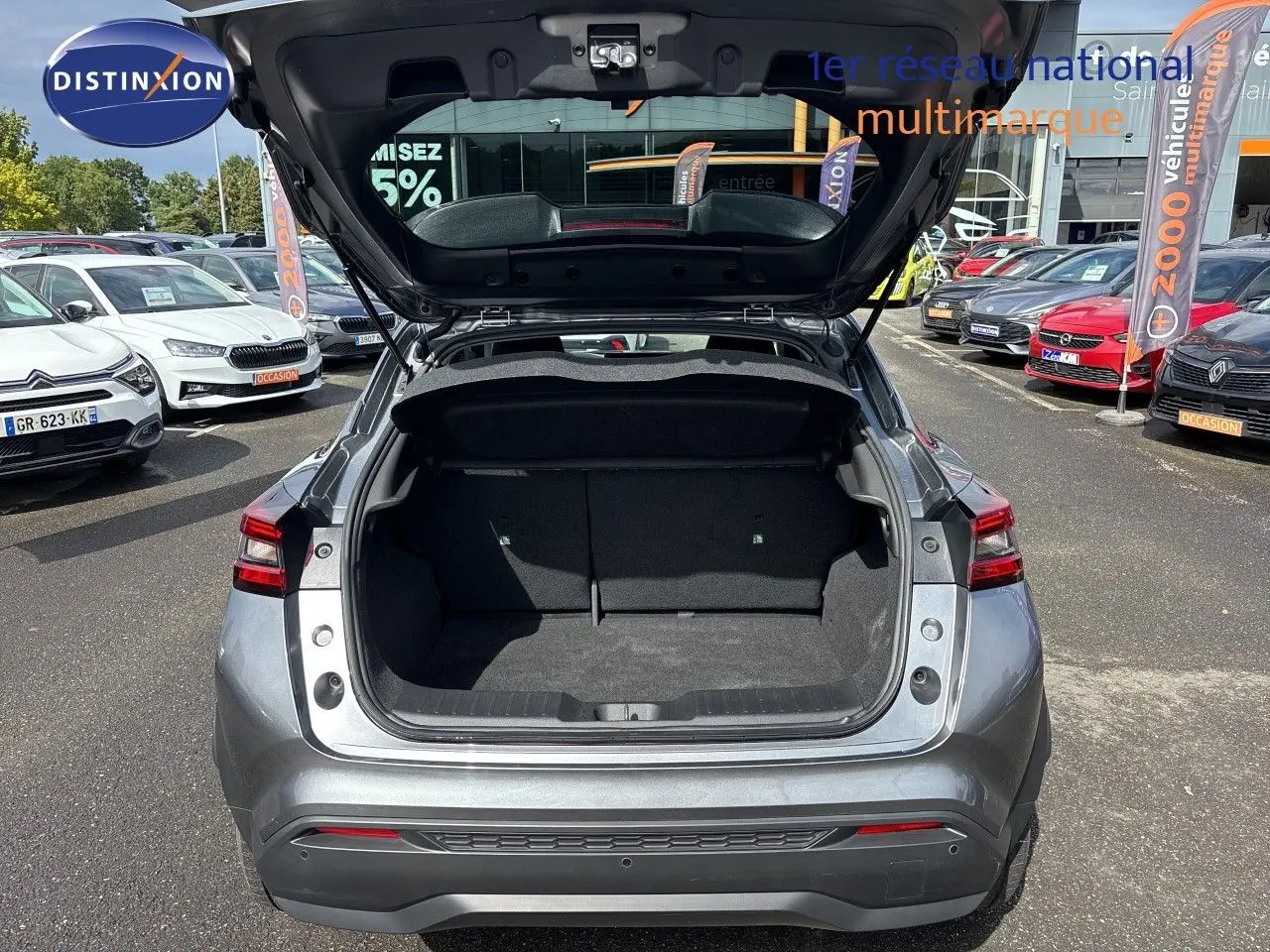 Vue arrière du Nissan Juke Hybrid gris squale métal 2024 avec coffre ouvert, montrant l’espace de chargement vide.