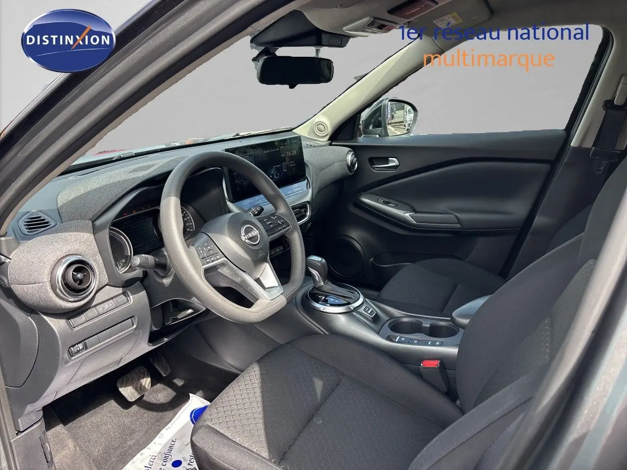 Vue intérieure côté conducteur du Nissan Juke Hybrid 2024 avec tableau de bord gris et sièges tissu noir.