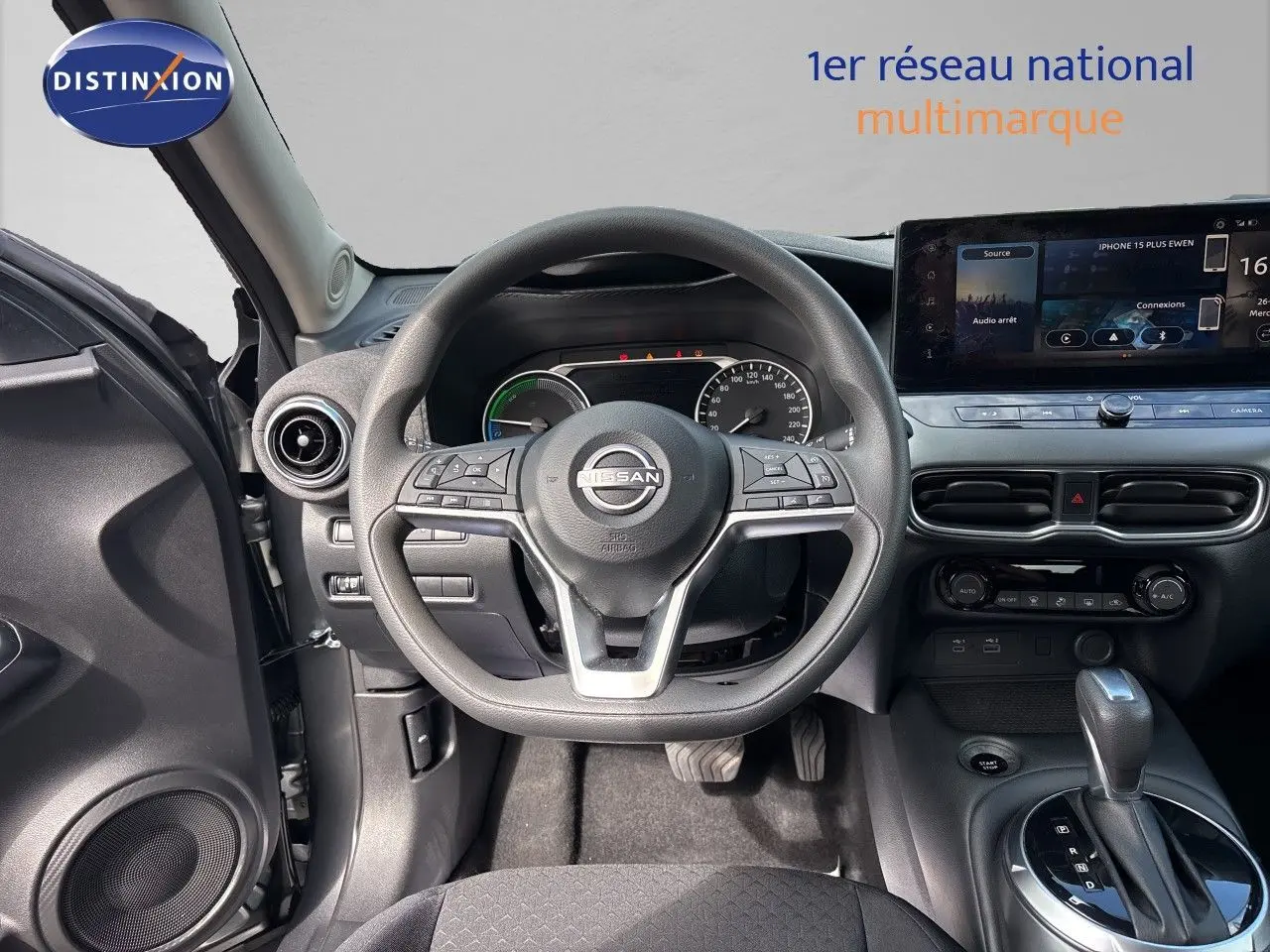 Vue intérieure centrée sur le volant et le tableau de bord du Nissan Juke Hybrid gris, avec écran tactile et levier de vitesse automatique.