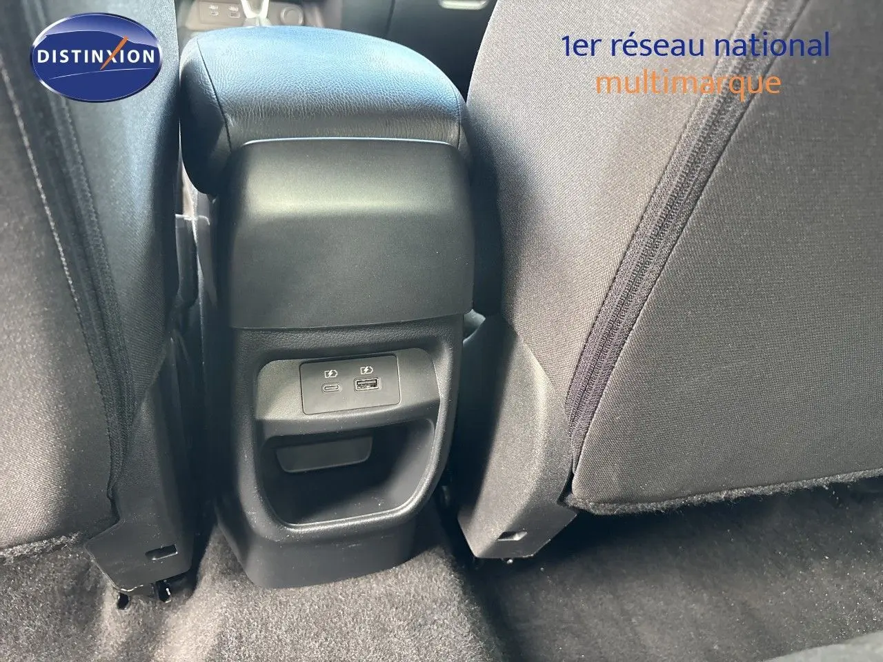 Vue rapprochée de la console centrale arrière du Nissan Juke Hybrid 2024, avec ports USB visibles et sièges tissu gris.