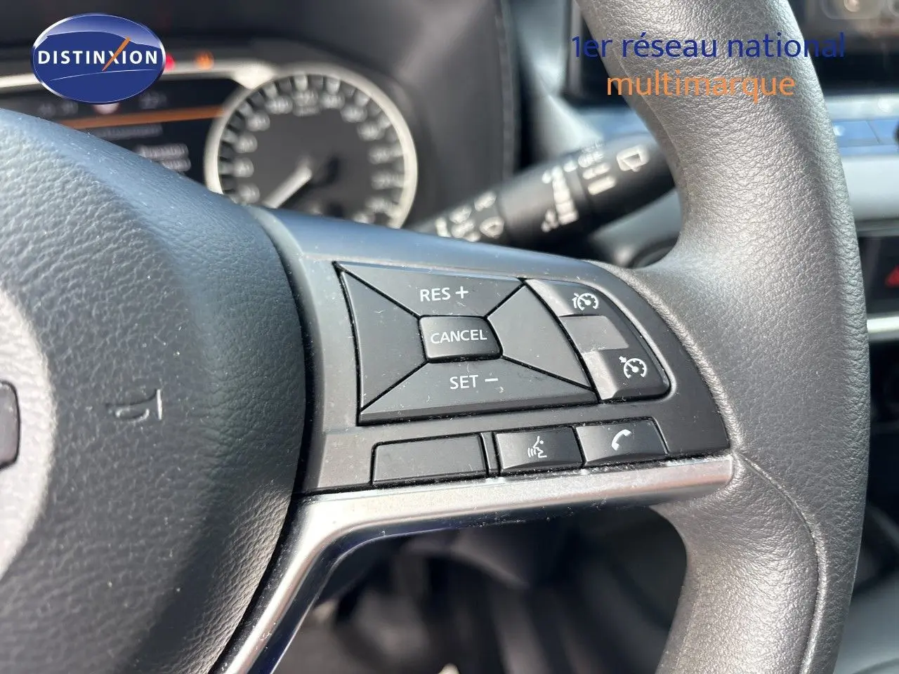 Gros plan sur les commandes au volant du Nissan Juke Hybrid 2024, avec tableau de bord flou en arrière-plan.