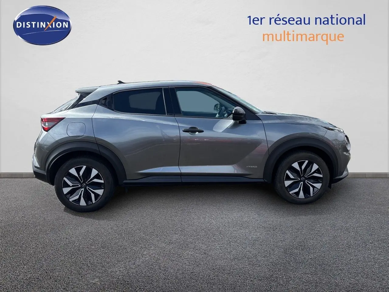 Profil latéral droit du Nissan Juke Hybrid 143ch Business Edition gris squale métal avec jantes noires et détails hybrides visibles.