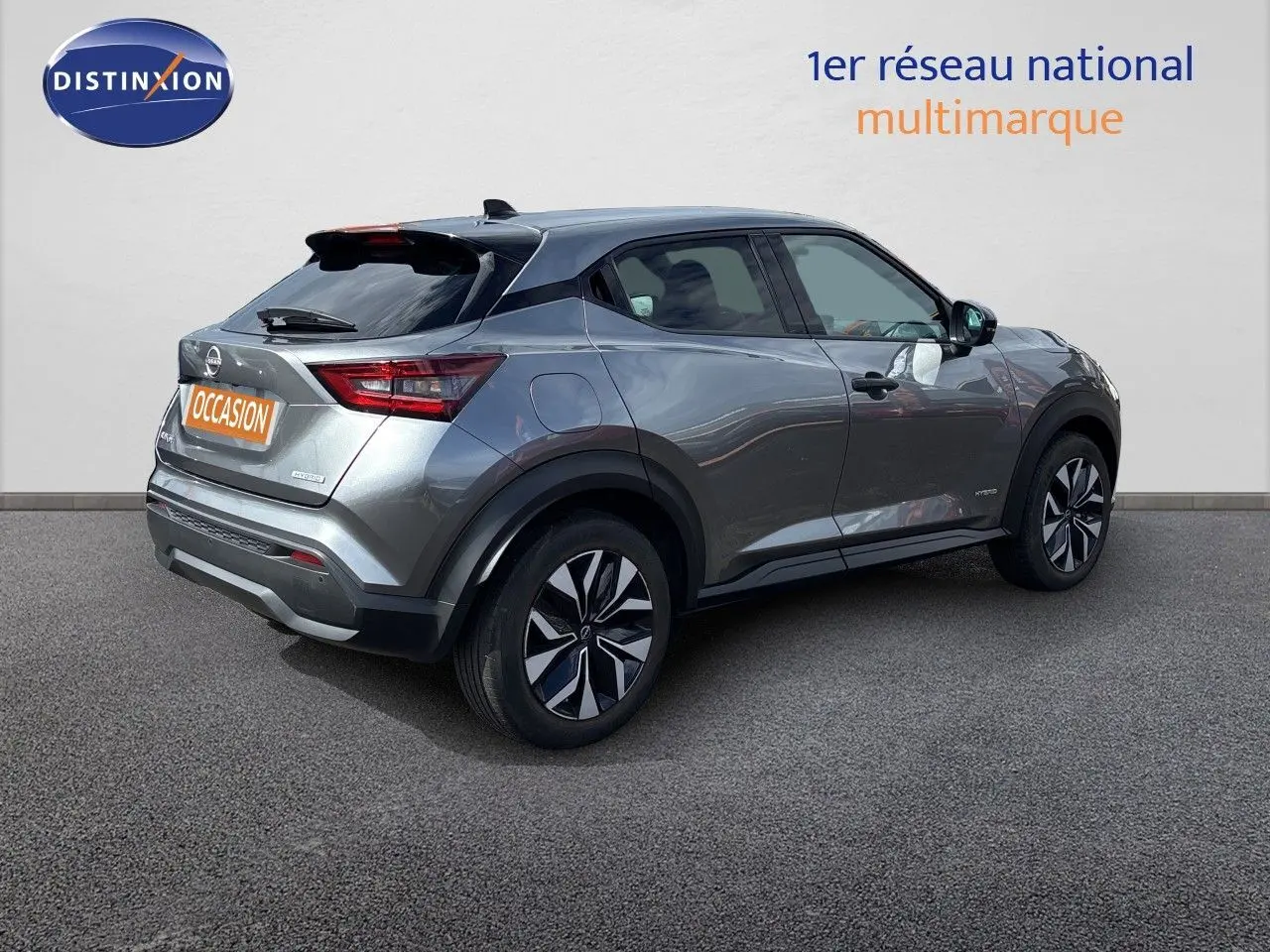 Nissan Juke Hybrid gris squale métal vu de trois quarts arrière droit, avec jantes noires et détails noirs contrastants.