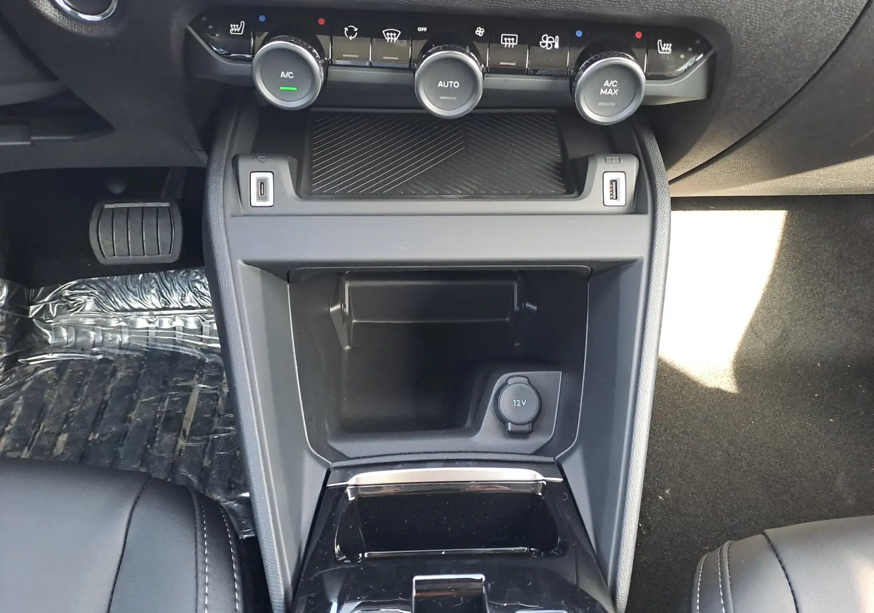 Vue rapprochée de la console centrale noire du Citroën C4 hybride 2025 avec commandes climatisation et prise 12V visible.