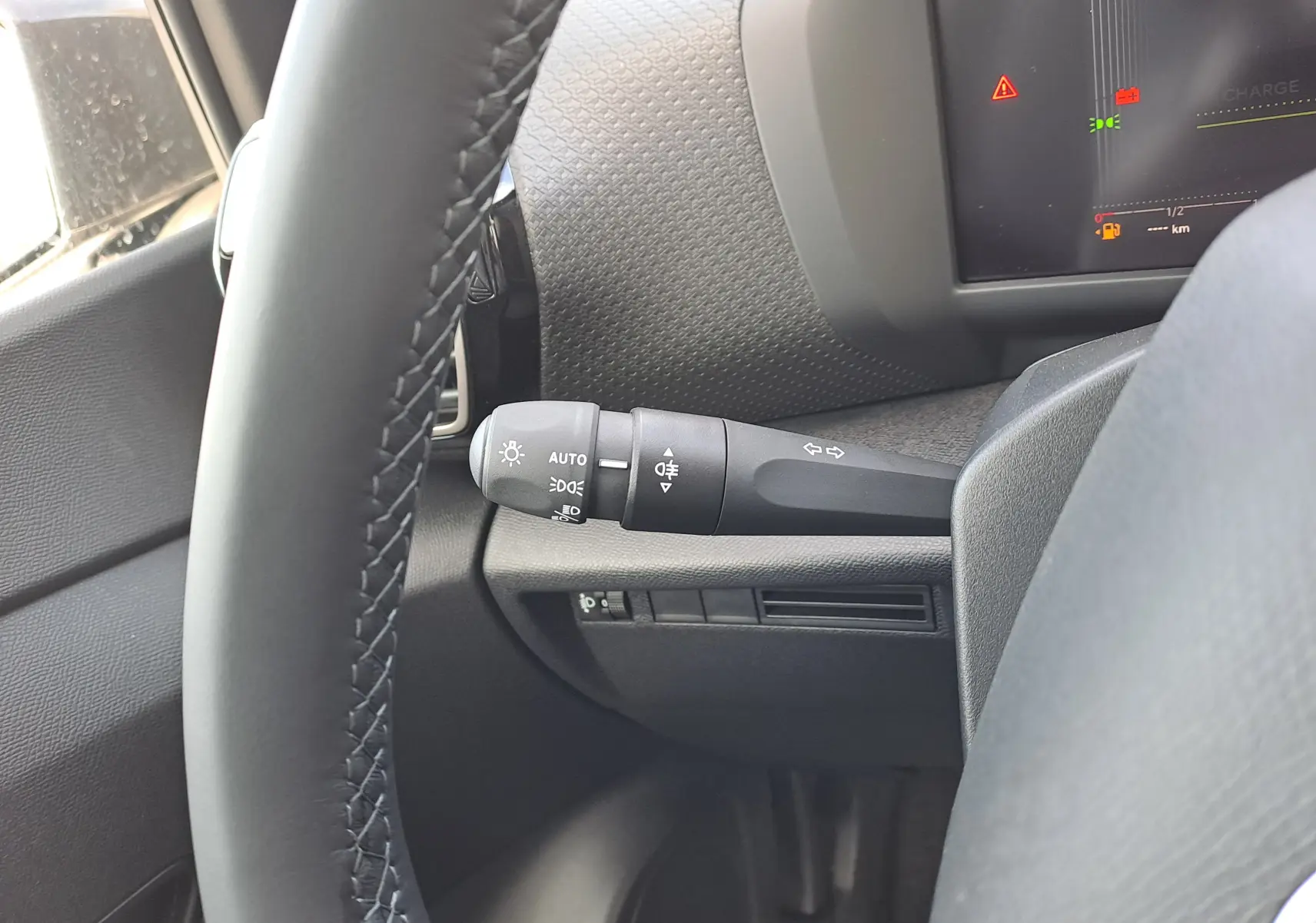 Gros plan sur la manette de clignotant et de feux à gauche du volant dans l'habitacle gris-noir de la Citroën C4 hybride.