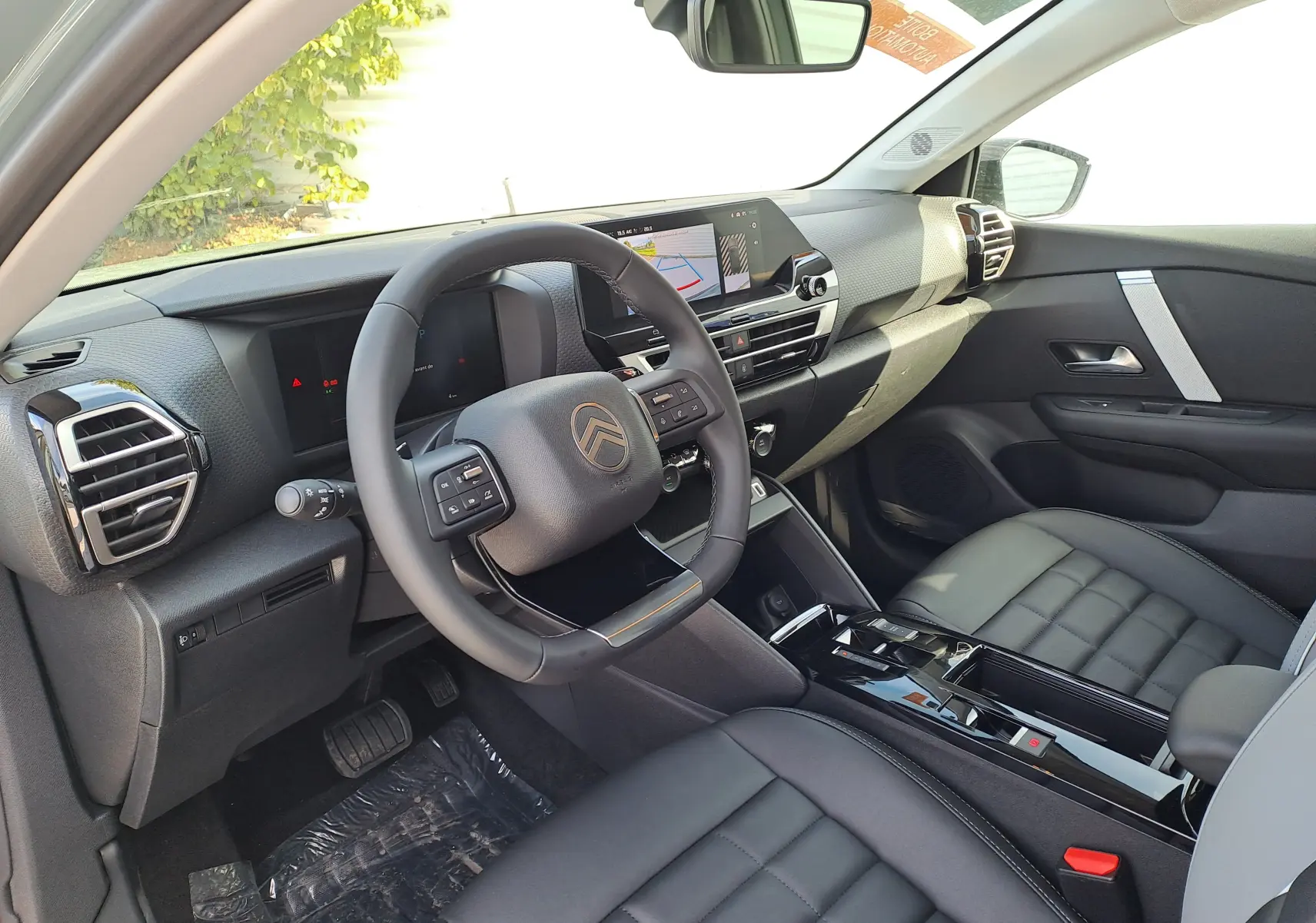 Vue intérieure côté conducteur de la Citroën C4 hybride 2025 avec tableau de bord noir et volant multifonction.