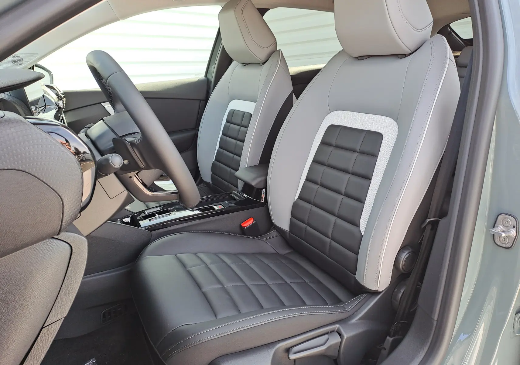 Vue intérieure côté conducteur de la CITROEN C4 hybride 2025 avec sièges bicolores gris clair et noir en cuir et tissu.