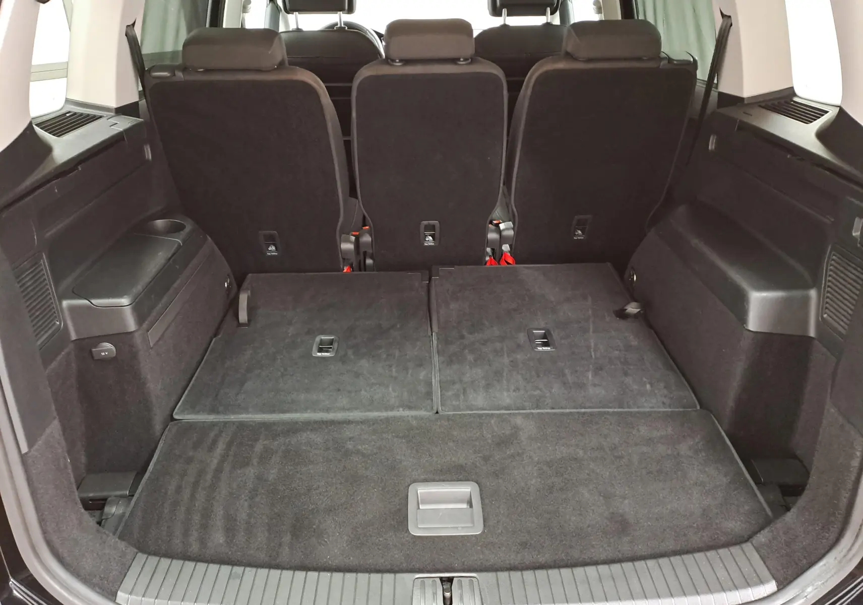 Vue arrière du coffre du Volkswagen Touran 2025 noir Grenadille avec sièges arrière partiellement rabattus et espace de chargement plat.