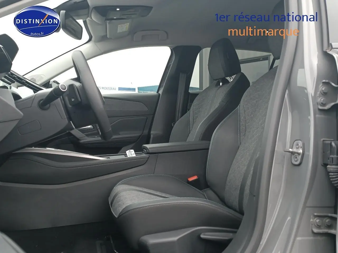 Vue intérieure côté conducteur de la Peugeot 408 Hybrid 145 allure gris sellenium, sièges bi-matière et accoudoir central visible.