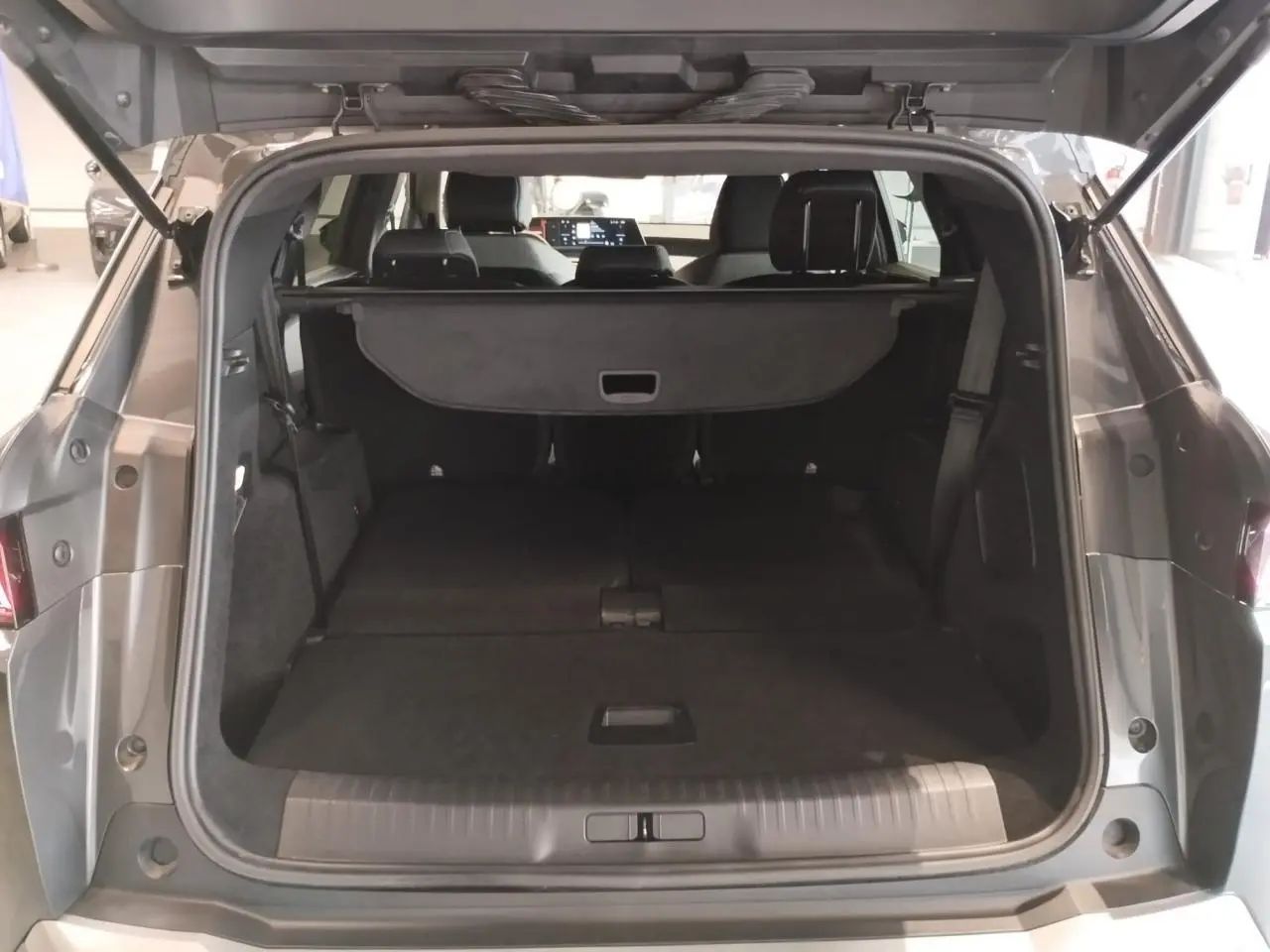 Coffre ouvert vu de l'arrière d'un Peugeot 5008 gris titanium avec banquette arrière rabattue et cache-bagages.