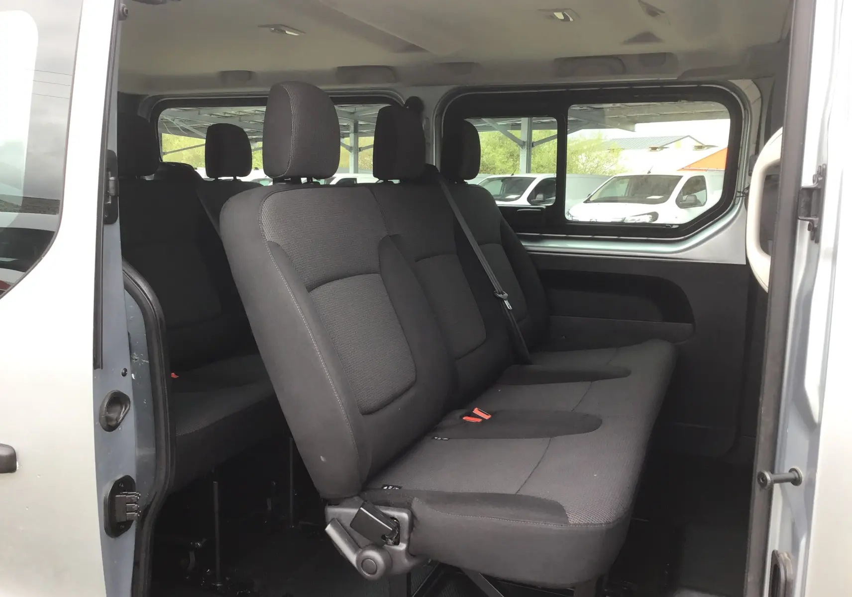 Vue intérieure côté droit sur les sièges noirs du Renault Trafic Combi gris clair, version 9 places avec porte coulissante ouverte.