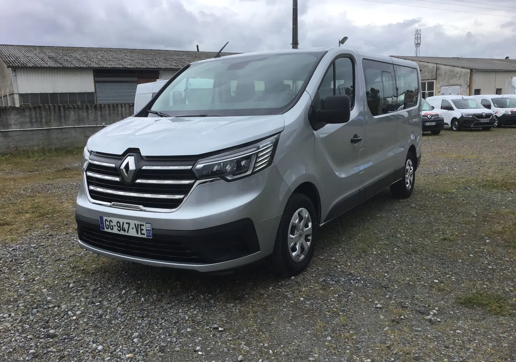 Renault Trafic Combi gris clair métal vu en 3/4 avant droit sur un sol gravillonné, avec calandre chromée et vitres teintées.