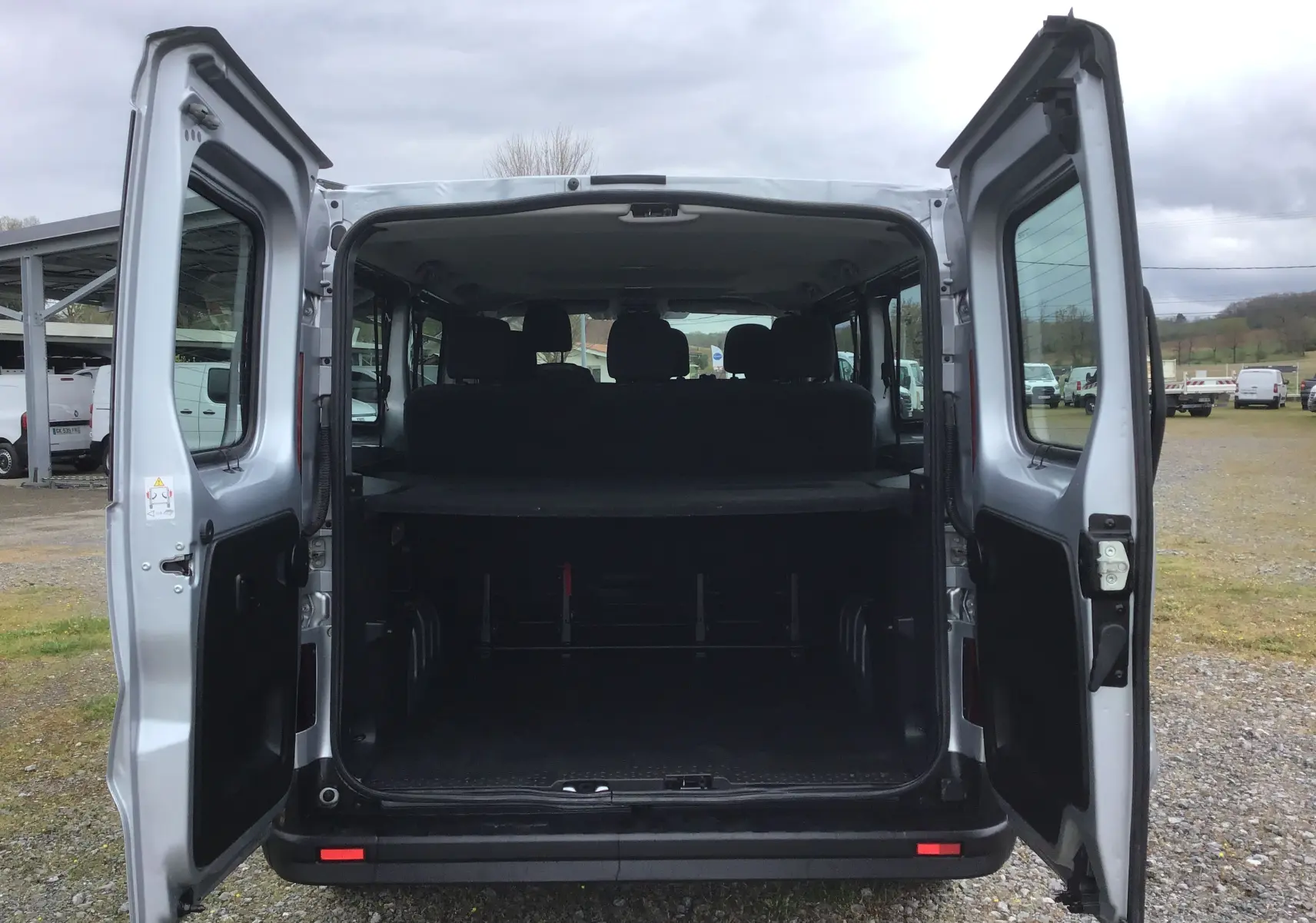 Vue arrière ouverte du Renault Trafic Combi gris clair métal montrant l'espace de chargement et les sièges arrière.
