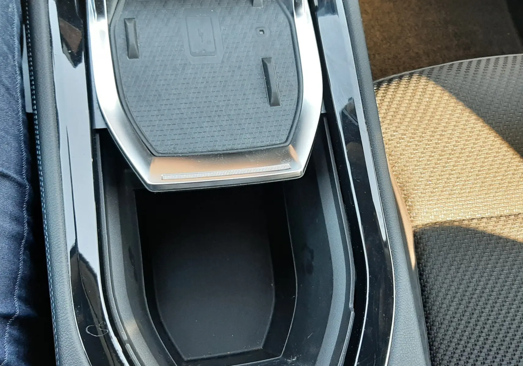 Gros plan sur la console centrale noire brillante du Renault Austral E-Tech 2025 avec espace de rangement et surface de charge sans fil.