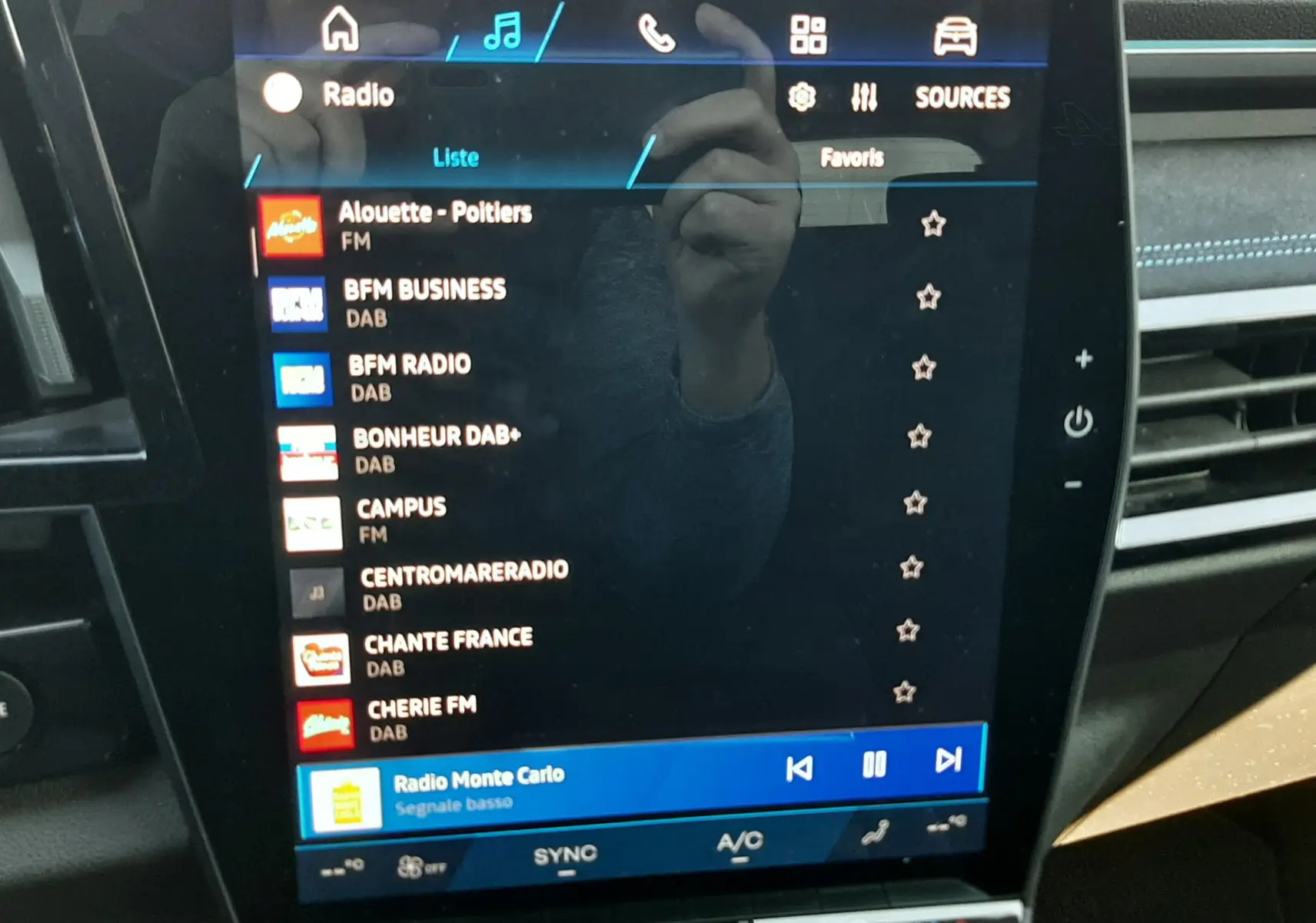 Écran tactile central du Renault Austral E-Tech hybride 2025 affichant la liste des radios, intérieur noir avec surpiqûres bleues.