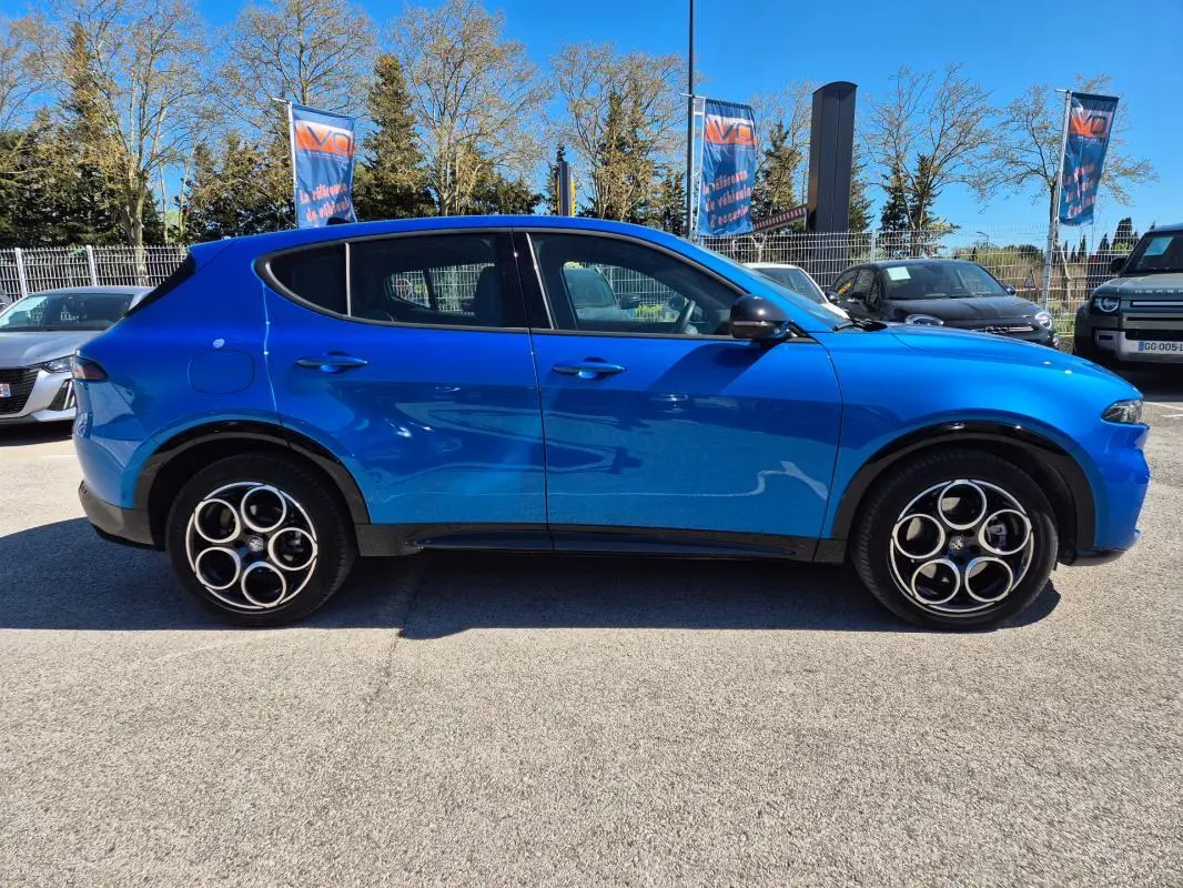 Vue de profil côté gauche d'un Alfa Romeo Tonale 1.5 Hybrid bleu avec jantes alliage 18 pouces sur parking extérieur.