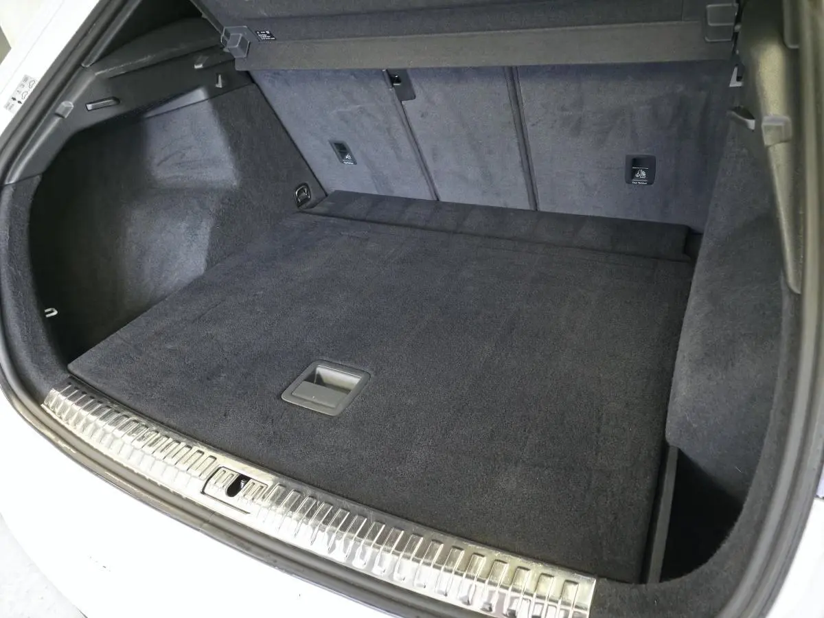 Coffre ouvert vu de l'arrière d'un Audi Q3 blanc, avec tapis de sol noir et seuil de chargement en métal.