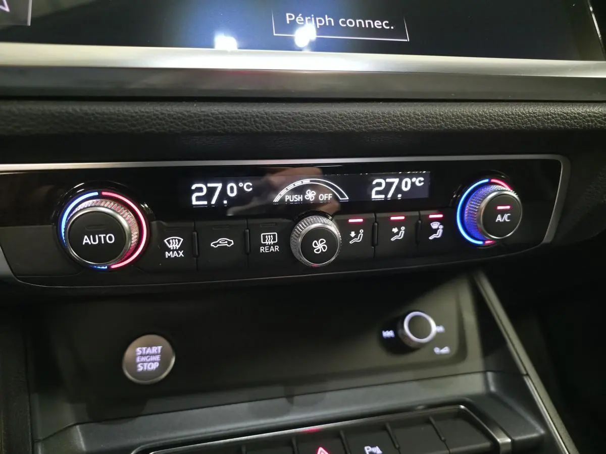 Détail de la console centrale de l’Audi Q3 blanc 2019, affichage de la climatisation à 27°C avec commandes tactiles et bouton start/stop.
