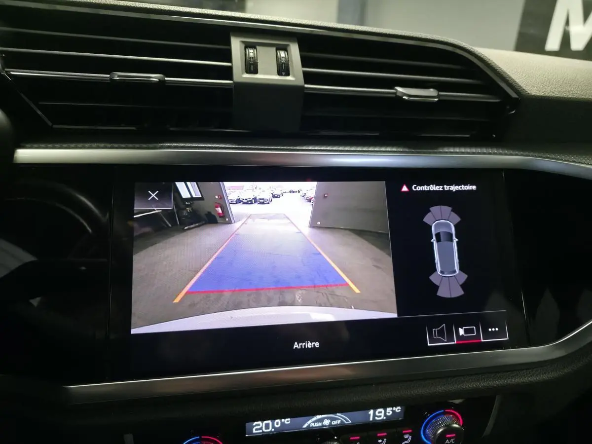 Écran central de l'Audi Q3 2019 blanc montrant la caméra de recul avec lignes de guidage et alertes de trajectoire.