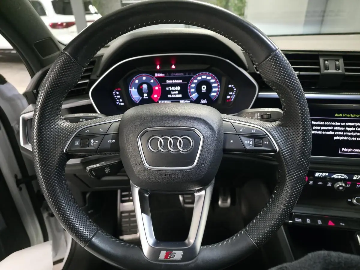 Vue rapprochée du volant sport S line noir perforé et du tableau de bord numérique d'un Audi Q3 2019.