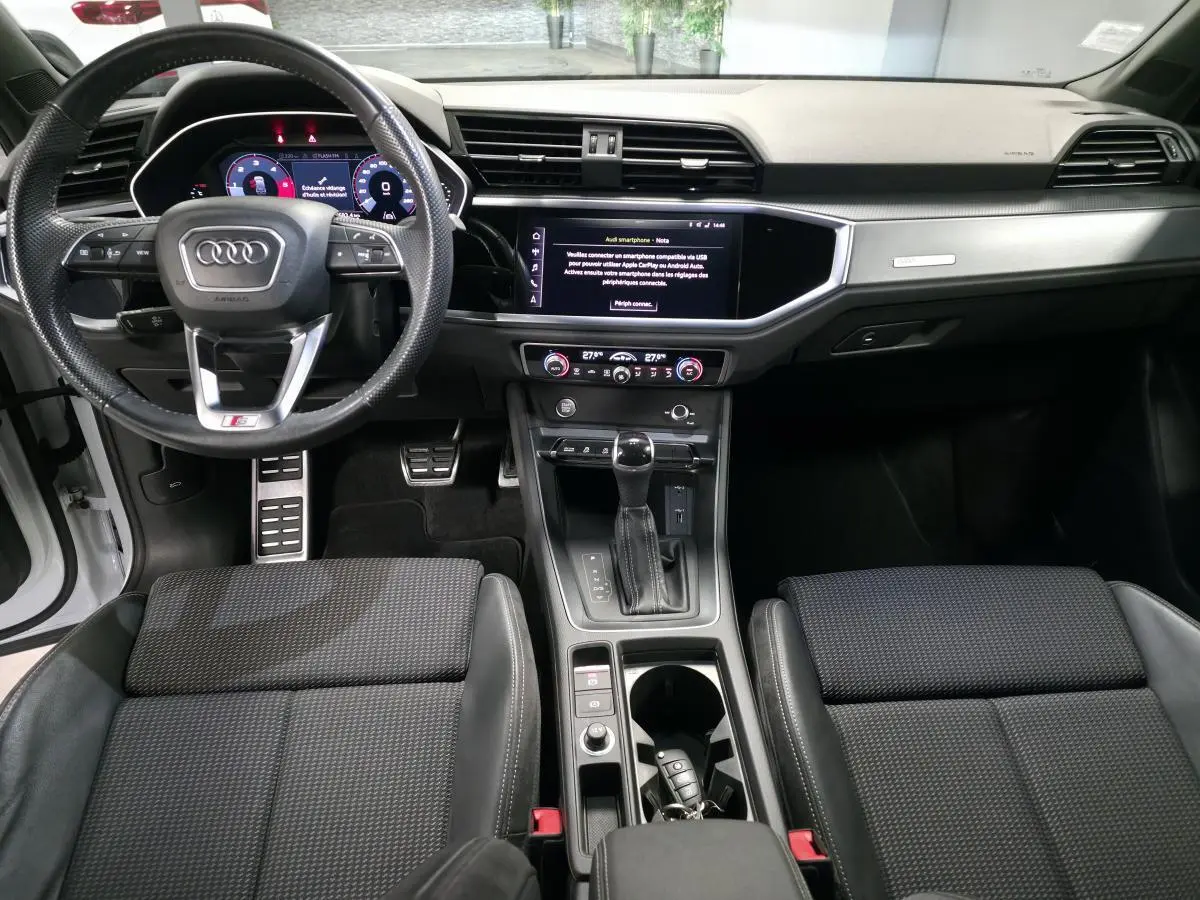 Intérieur Audi Q3 S-Line 2019 vu de face, tableau de bord noir avec écran tactile et volant sport multifonction.