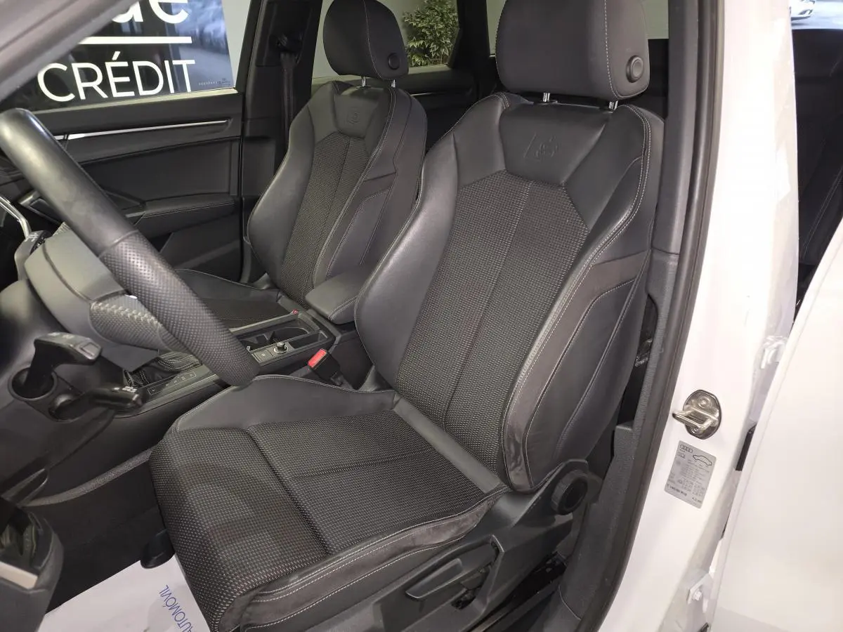 Vue intérieure côté conducteur de l'Audi Q3 blanc, mettant en valeur les sièges sport S line en cuir noir avec logo embossé.