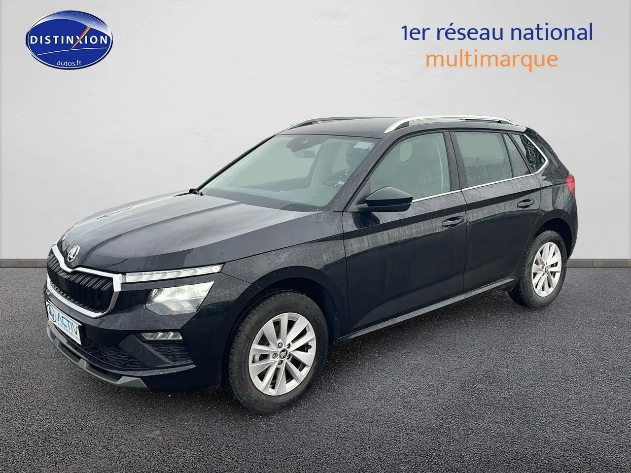 Vue 3/4 avant d’un Skoda Kamiq noir 2025 avec jantes alu et barres de toit argentées sur fond neutre.
