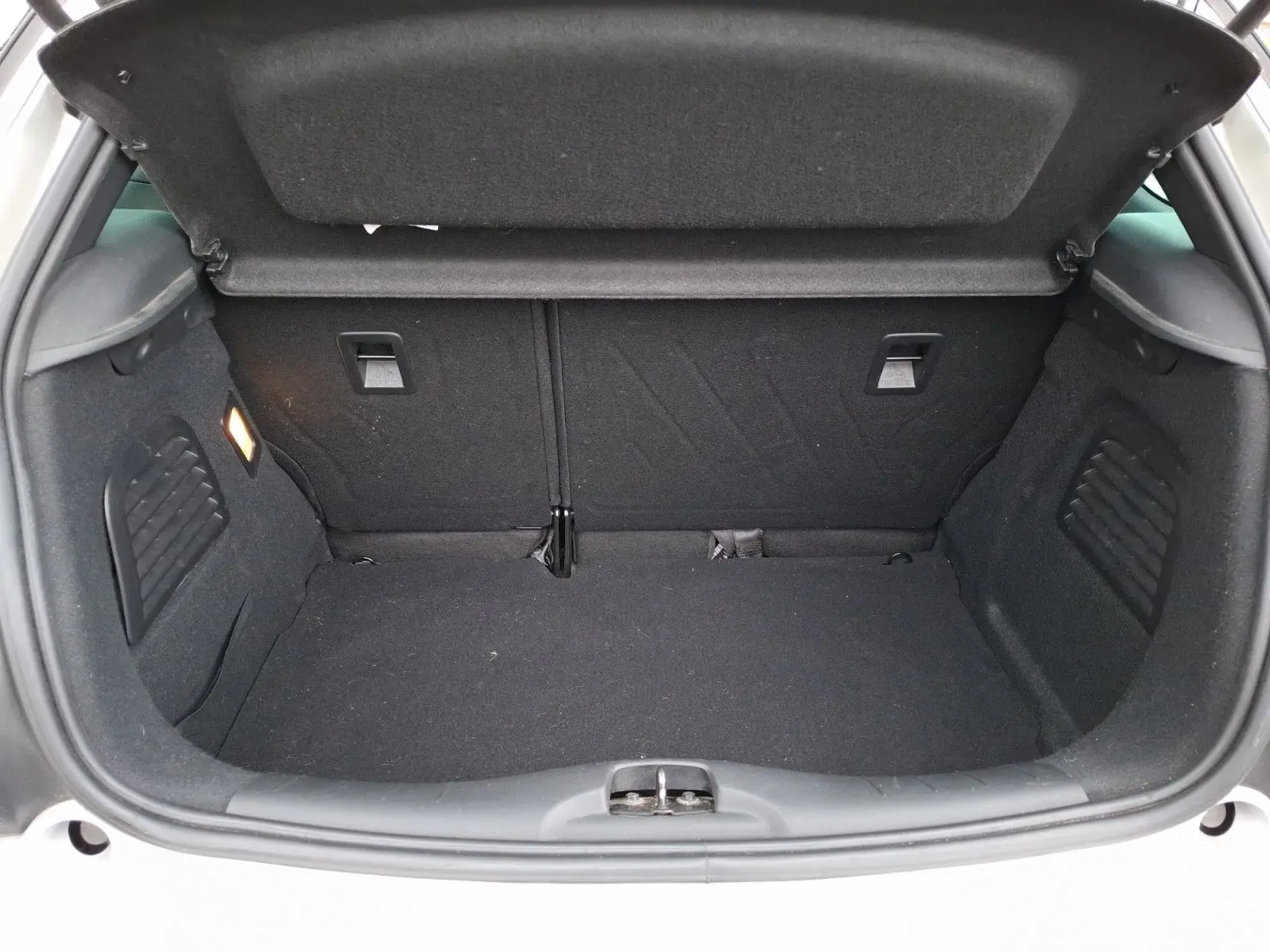 Coffre ouvert vu de l’arrière d’une Citroën DS3 gris clair, montrant l’espace de chargement vide et la moquette noire.