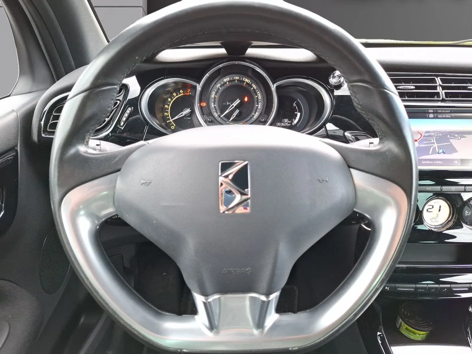 Vue rapprochée du volant et du tableau de bord d'une Citroën DS3 gris clair avec écran GPS et commandes intégrées.