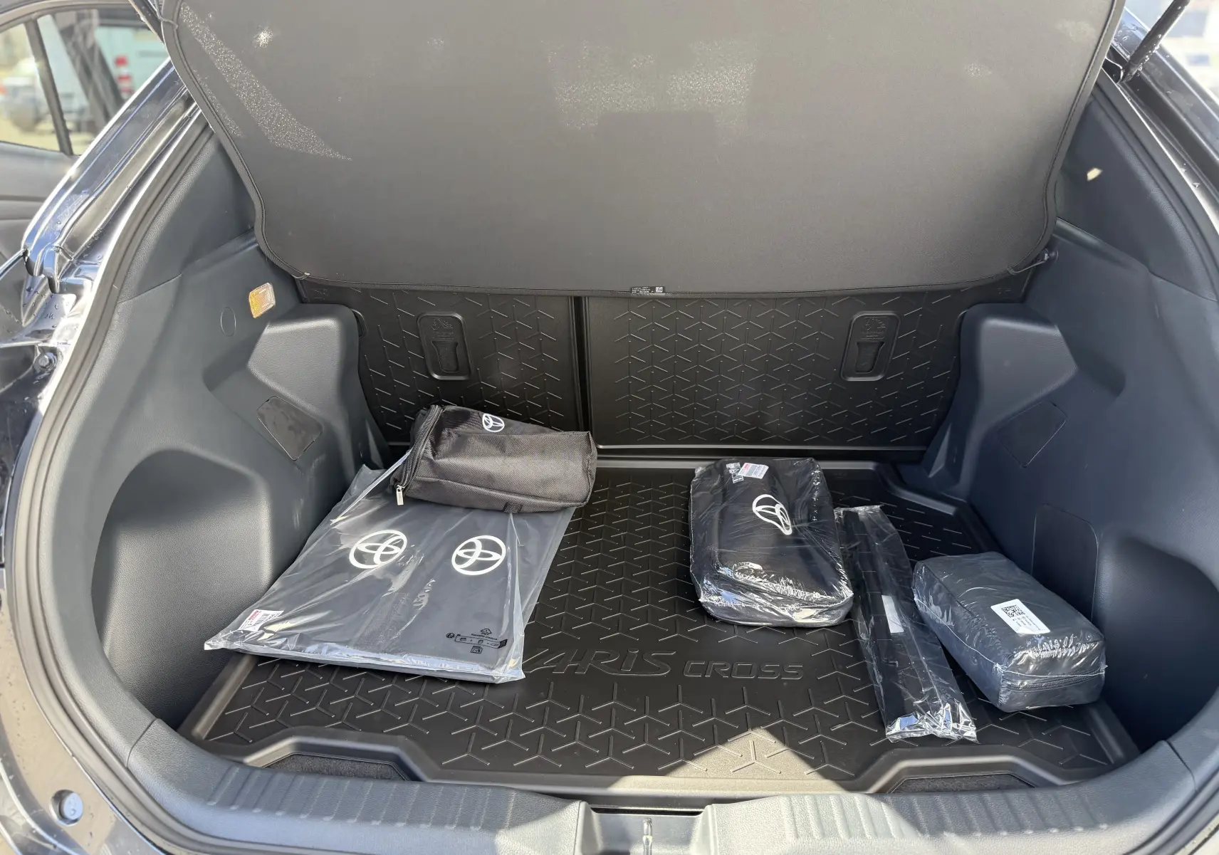 Coffre ouvert vu de l'arrière d'une Toyota Yaris Cross gris atlas, avec tapis de coffre et accessoires Toyota visibles.