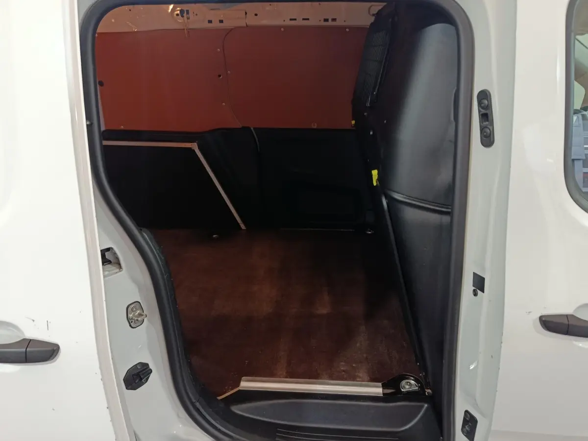 Vue intérieure côté droit du coffre vide d’un utilitaire Citroën Berlingo blanc avec cloison pleine noire.