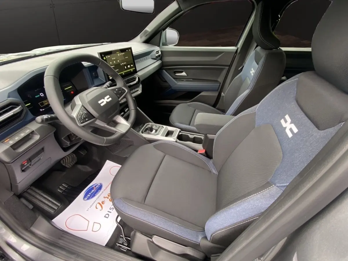 Vue intérieure côté conducteur du Dacia Duster Journey Hybrid 140, sièges noirs avec inserts bleus et tableau de bord moderne.