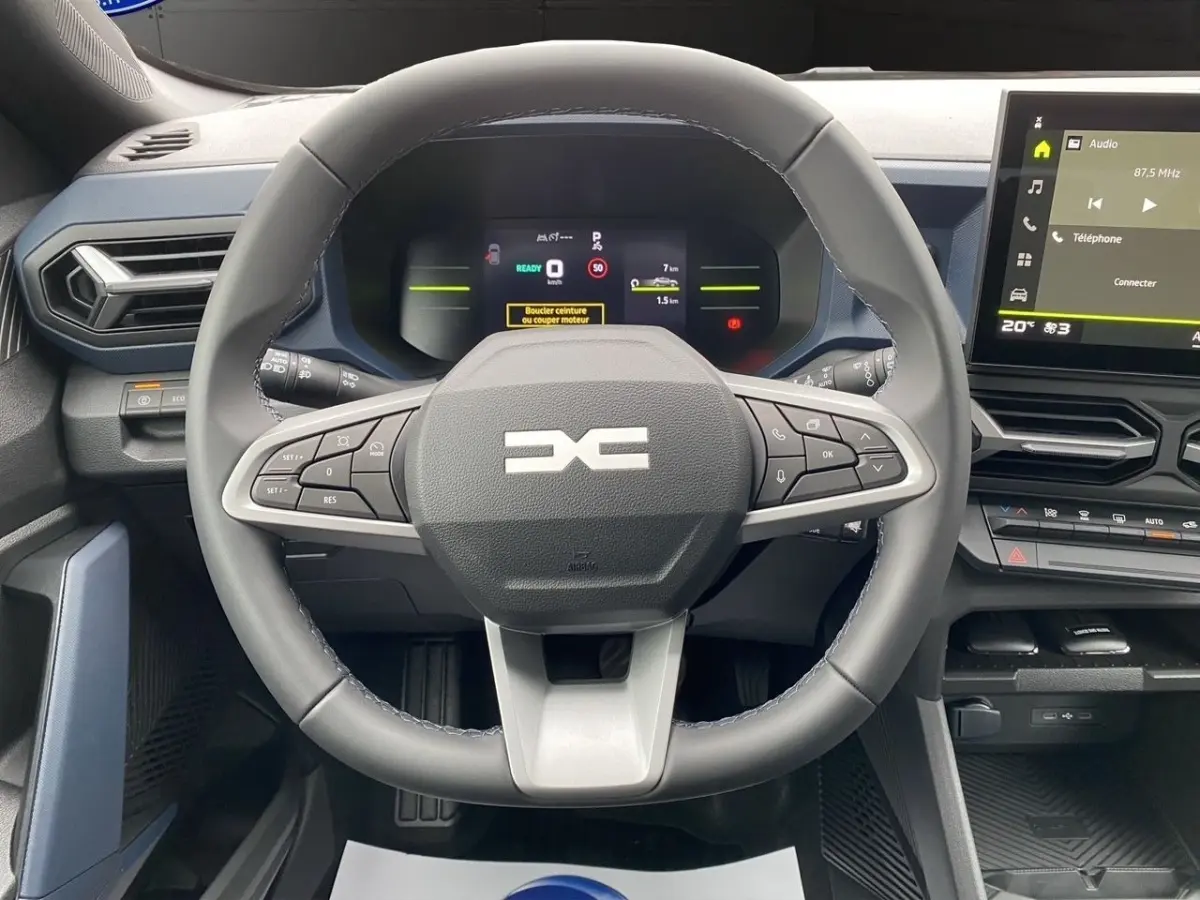 Vue intérieure centrée sur le volant multifonctions et le tableau de bord numérique du Dacia Duster gris foncé.